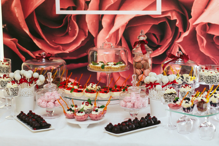 Pastry and other swetts stand on a white table behind a pink wallの写真素材