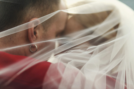 A closeup of a wedding couple hugging under a veil