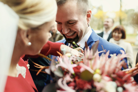 Groom laughs while bride adjusts a veil on his jacketの写真素材
