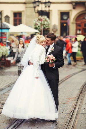 Groom holds a bride in his hugs standing on the tramwaysの写真素材