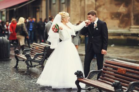 Groom kisses bride's hand standing between benches on an old streetの写真素材