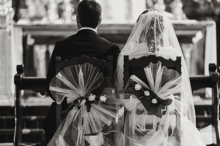 Bride and groom sit on the wooden chairs decorated with flowersの写真素材