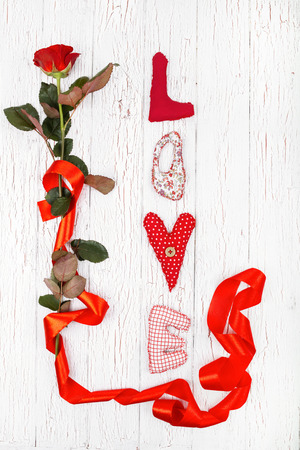 the word "love" and a red rose with a ribbon lie on white surfaceの写真素材