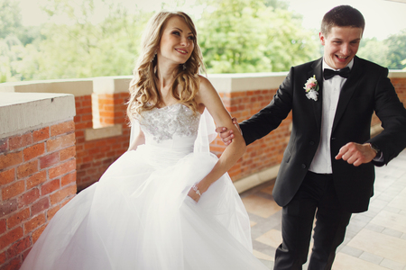 Groom runs along a balcony holding bride's handの写真素材
