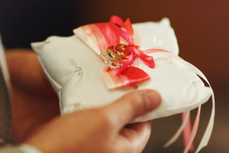 Man holds a pillow with wedding rings decorated with red and white bows
