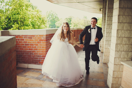 Bride smiles holding groom's hand and running with him along the balconyの写真素材