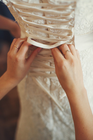 Bridesmaid laces up a corset of a wedding dressの写真素材