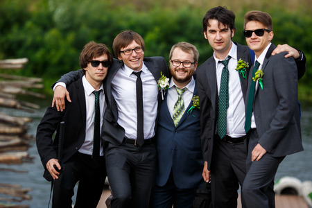 Stylish dressed groom and groomsmen pose together by the riverの写真素材