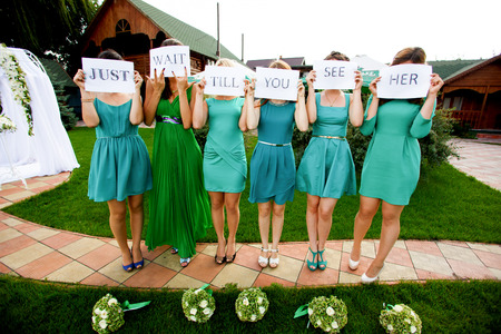 Bridesmaids hold a lettering 'Just wait till you see her' printed on white papers behind their facesの写真素材