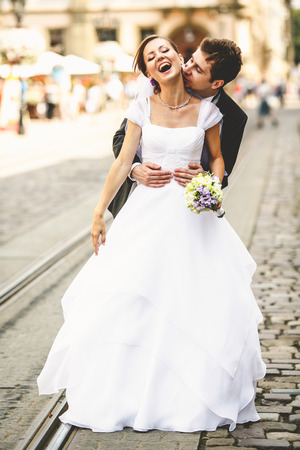 Bride laughs while groom kisses her neck somewhere in the old townの写真素材