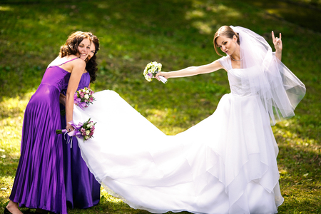 Bride makes rock'n'roll while pretty bridesmaids carry her dressの写真素材
