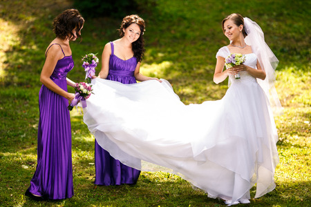 Bridesmaids spread bride's dress standing on the grass in parkの写真素材