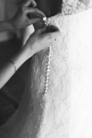 Delicate woman's hands button up a wedding dressの写真素材