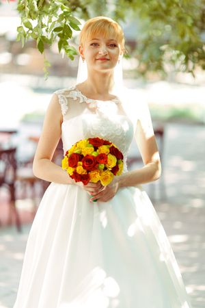 Bride smiles standing with a bouqet on a street in shiny morningの写真素材