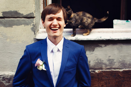 Little cat cathes fiance's ear while he stands behind an open windowの写真素材