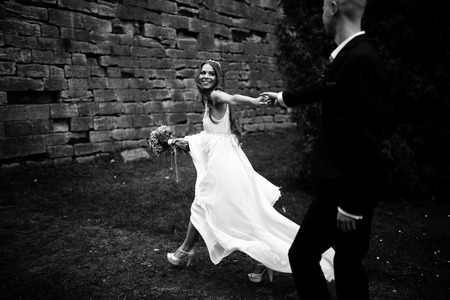 A black and white picture of a stunning bride walking along the stone wall with a groomの写真素材