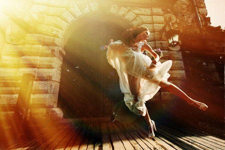 Bride jumps up in the air before an old castle in the sunraysの写真素材