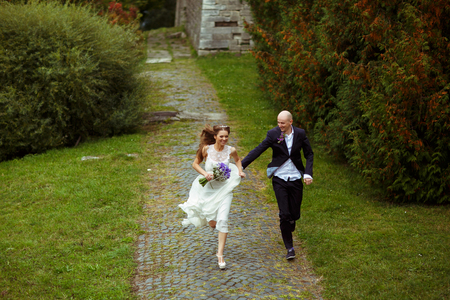 Smiling wedding couple run along the parkの写真素材