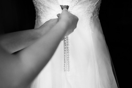 Woman's hands buttons up a white dressの写真素材