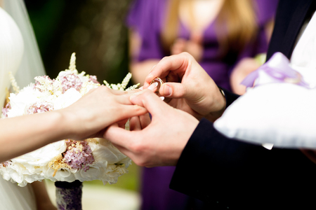 Groom puts a wedding ring on bride's delicate fingerの写真素材