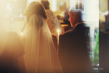 A view from behind on groom and bride praying with candles in their arms during a ceremony