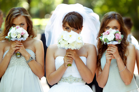 Bride and bridesmaids hide their faces behind little wedding bouqeutsの写真素材
