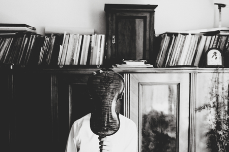 Man hidden behind a violin stands in the front of an old wardrobeの写真素材