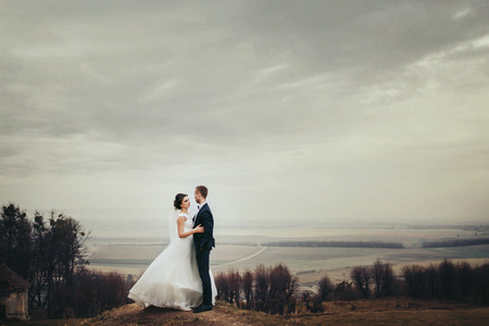 Bride and groom stand on the hill with great autumn landscape behind themの写真素材