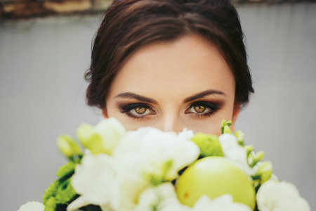 Brunette bride with magic green eyes looks over a green wedding bouqetの写真素材