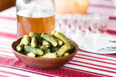 Pickled cucumbers stand on the table behind empty glasswareの写真素材