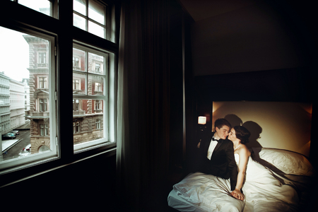 Bride and groom sit on the bed in a dark roomの写真素材