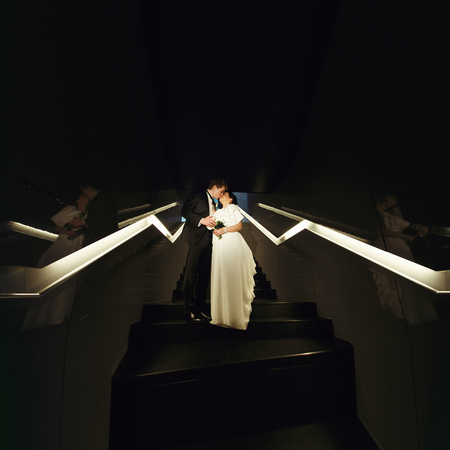 Newlyweds kiss standing on the stairs illuminated with neon lightsの写真素材