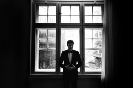 Man in a tuxedo stands thoughtful in the front of a bright windowの写真素材