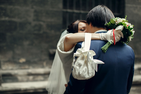 A little cloth bag hands from the bride's wrist while she hugs a groomの写真素材