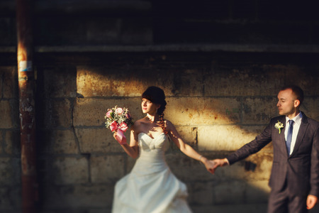 Bride looks at a sun holding a bouqet in one arm and groom's hand in anotherの写真素材
