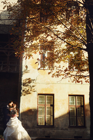 Bride and groom kiss standing in the front of a builidng illuminated by the sunの写真素材