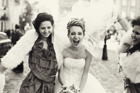 Bridesmauds raise bride's veil while they dance on the streetの写真素材