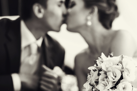Wedding bouquet lies on the frontground of a black and white picture of kissing newlywedsの写真素材