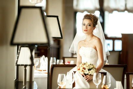 Tender young bride stands between chairs in an empty restaurant hallの写真素材