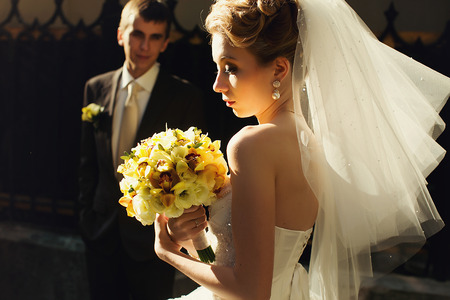 Groom admires a bride standing on the background while she walks in the morning lightsの写真素材