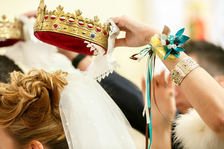 Bridesmaids hand decorated with flower bracelet holds a crown over a brideの写真素材