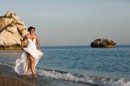 Bride raises her dress up walking in the sea waterの写真素材