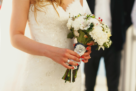 Bride holds in her tender hands a wedding bouquet decorated with a ropeの写真素材