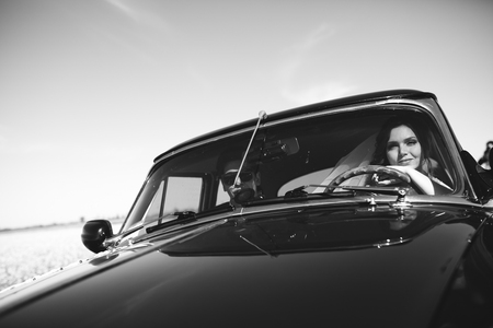 Smiling newlyweds sit in an old car in a sunny dayの写真素材