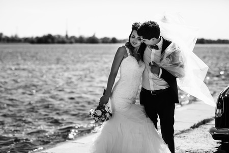 Awesome bride leans to groom's shoulder while posing by the seaの写真素材