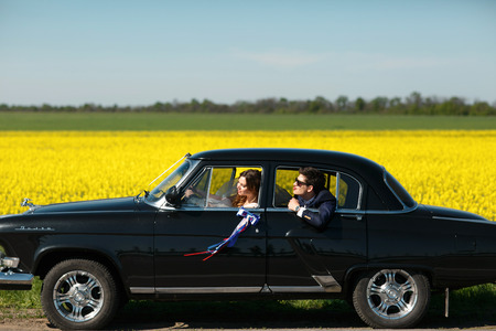 Groom tries to reach a bride from the back seat of an old carの写真素材