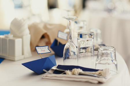 Little blue paper ships lie behind the glassware on a dinner tableの写真素材