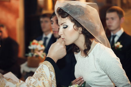 Classy bride kisses a wedding ring held by a priestの写真素材