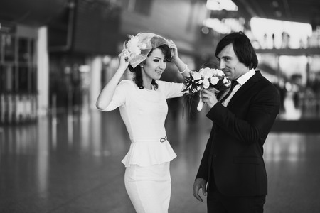 Groom smells a wedding bouquet standing behind a bride in the airport terminalの写真素材