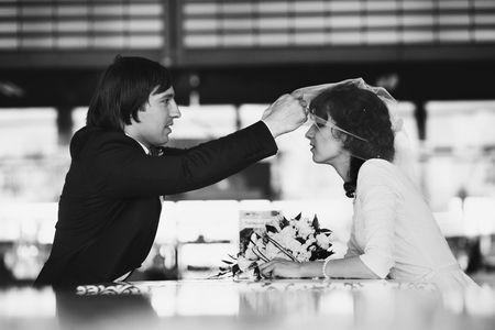 Groom raises bride's veil while they sit in the cafeの写真素材